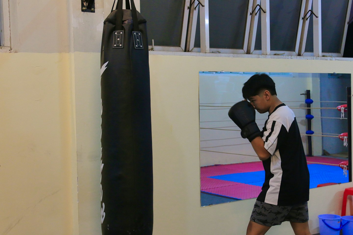 Boxer in gloves practices stances before a mirror in a gym.