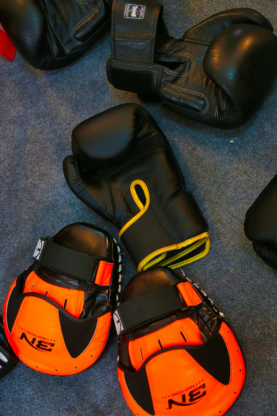 Boxing gloves and training mitts resting on a carpeted floor.