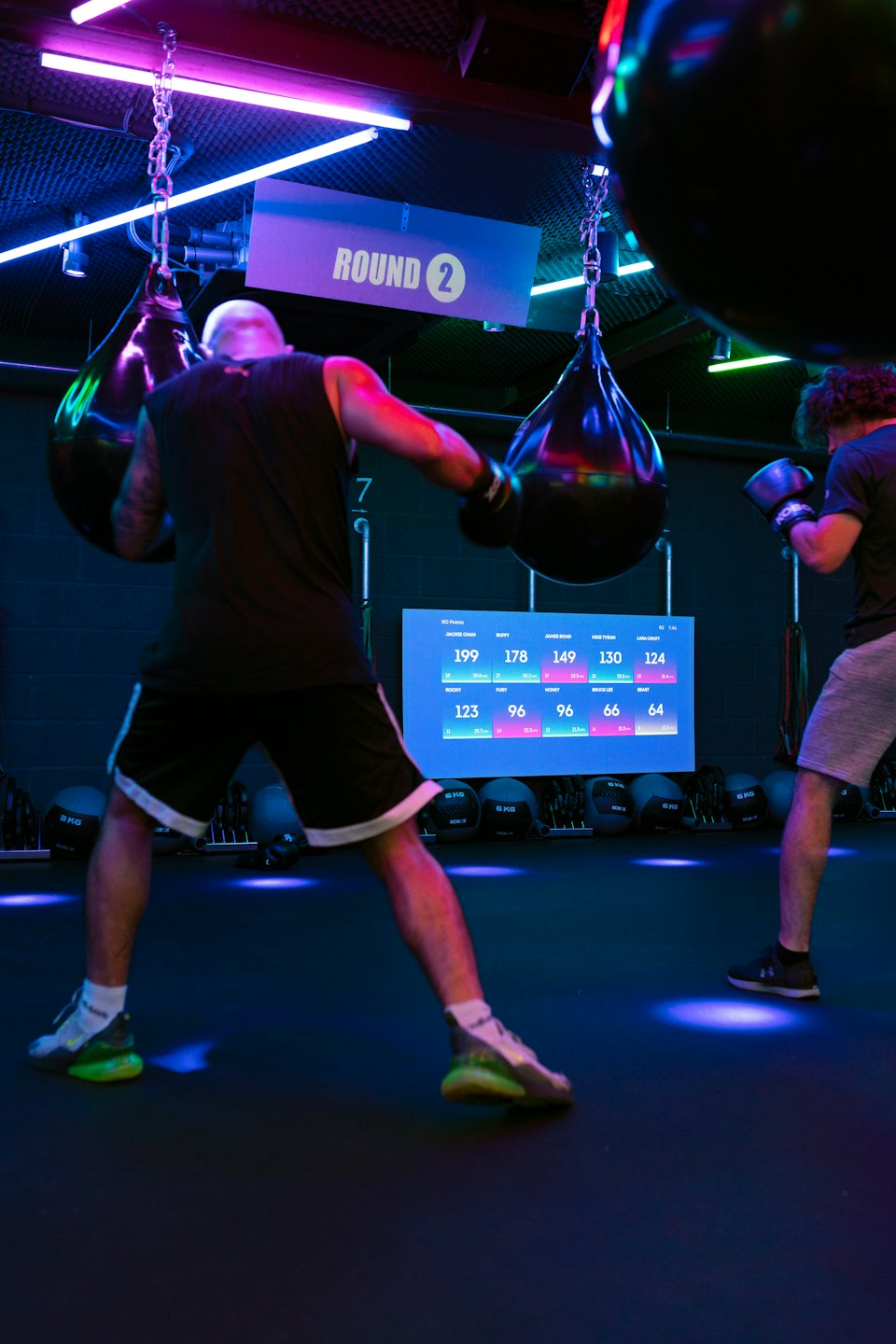 Two men train with boxing bags in a modern gym.